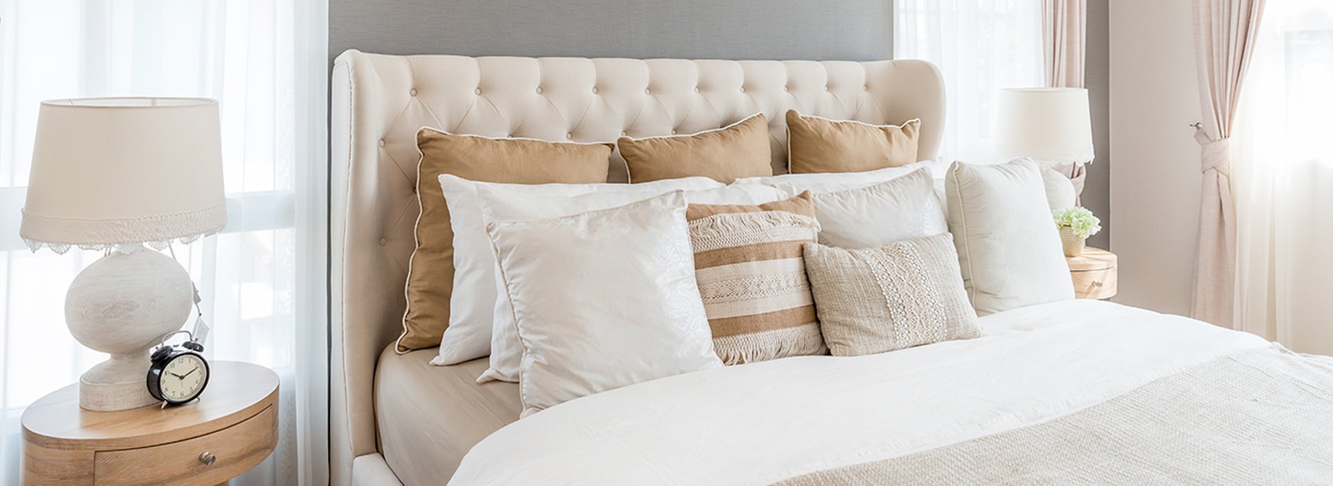 Patterned-pouf-and-basket-in-bright-bedroom-interior-with-lamps,-plants-and-poster-next-to-bed